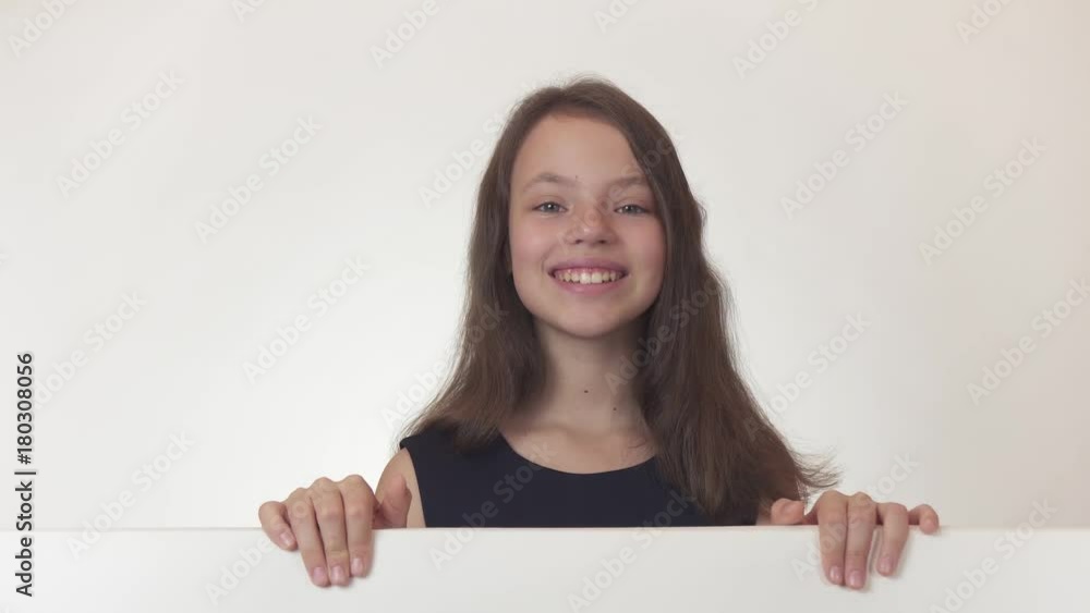 Beautiful girl teenager holds a poster with information and joyfully advertises it on white background stock footage video. Beautiful girl teenager holds a poster with information and joyfully advertises it on white background stock footage video.