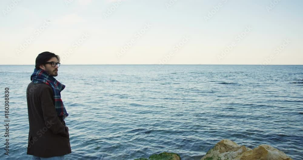 Back view on a handsome man standing on the seacoast and looking opposite the sea. Cloudy cold weather. Outdoor. Back view on a handsome man standing on the seacoast and looking opposite the sea. Cloudy cold weather. Outdoor.
