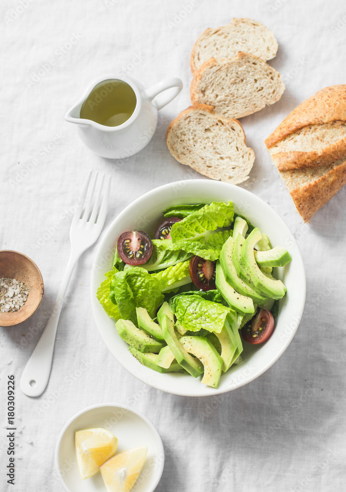Avocado, romano, kumato tomatoes salad and whole wheat branny bread on light background, top view. Healthy diet vegetarian food concept Avocado, romano, kumato tomatoes salad and whole wheat branny bread on light background, top view. Healthy diet vegetarian food concept