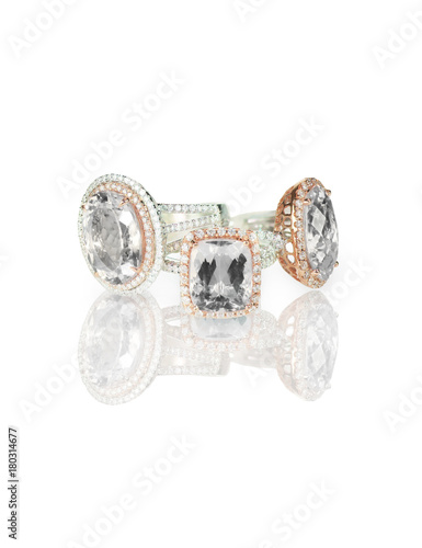 Fototapeta Naklejka Na Ścianę i Meble -  A grouping set of beautiful diamond halo  cushion cut center stone engagement/wedding/fashion rings in a rose gold or brass halo setting isolated on white with a shadow and reflection.
