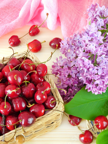 Cherries in a basket and a blooming branch of lilac on a wooden table