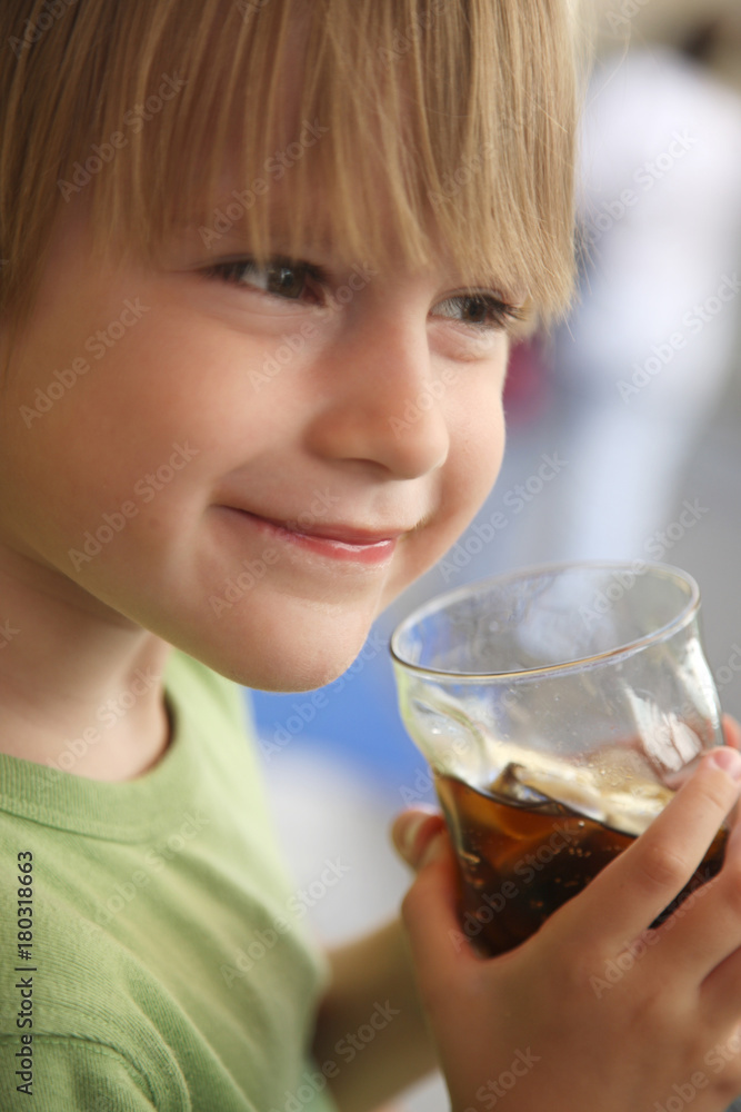 A child with a smile on his face holding a glass with a refreshing drink in hand A child with a smile on his face holding a glass with a refreshing drink in hand