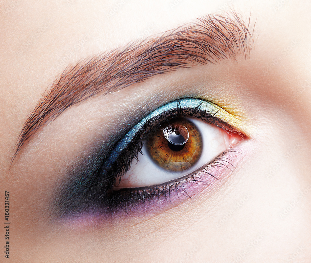 Closeup macro shot of human female eye. Girl with perfect skin and lilac - blue - yellow eyes shadows