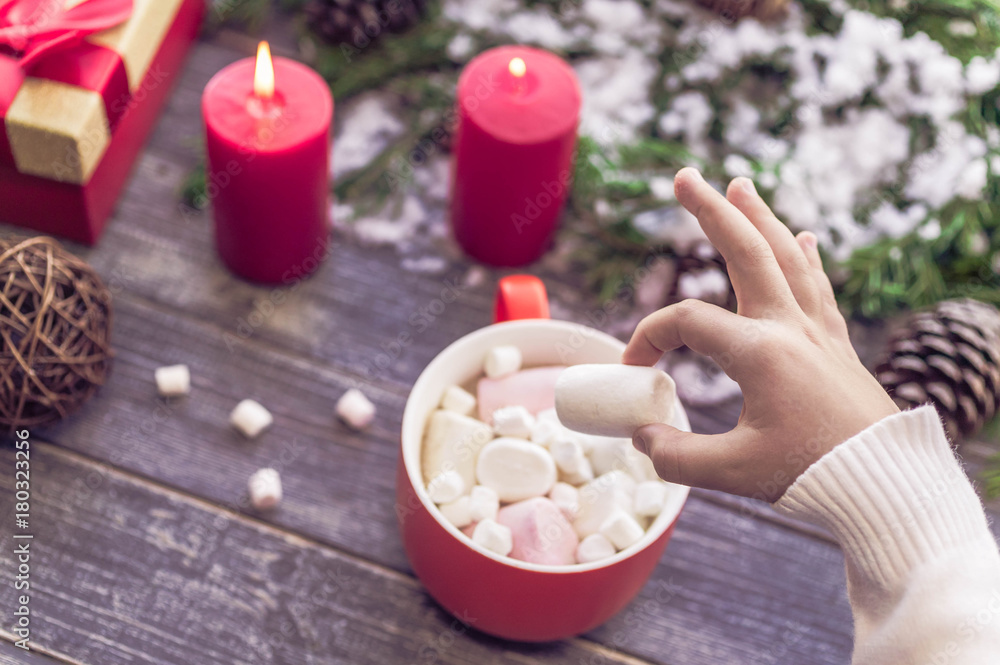 Christmas still life. Children's hands hold big marshmallows. A cocoa cup from marshmallows on a wooden table against the background of the New Year's still life. Selective focus Christmas still life. Children's hands hold big marshmallows. A cocoa cup from marshmallows on a wooden table against the background of the New Year's still life. Selective focus
