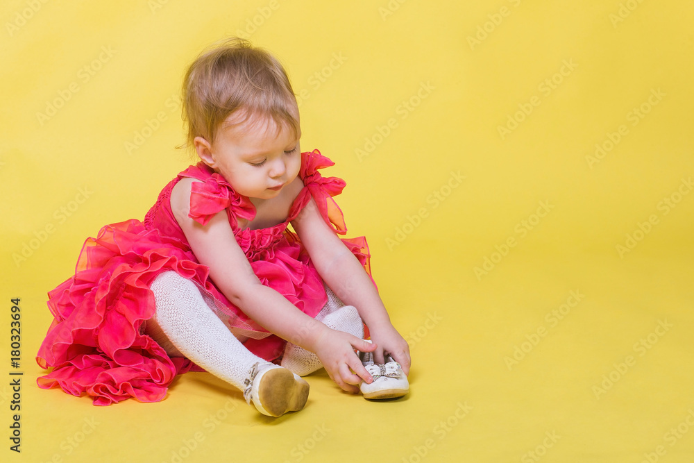 Naklejka premium Girl toddler in a pink dress on a yellow background wearing the shoes on his feet