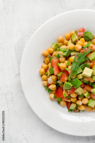 Vegan salad with chickpeas, tomato and avocado on white concrete table. Vertical photo.