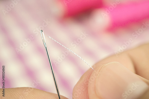 Finger hold white thread focus to push through the sewing needle hole