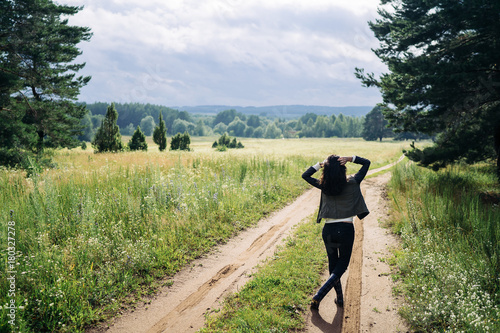 Young woman in rain boots is walking along country road at sunset on a moody day