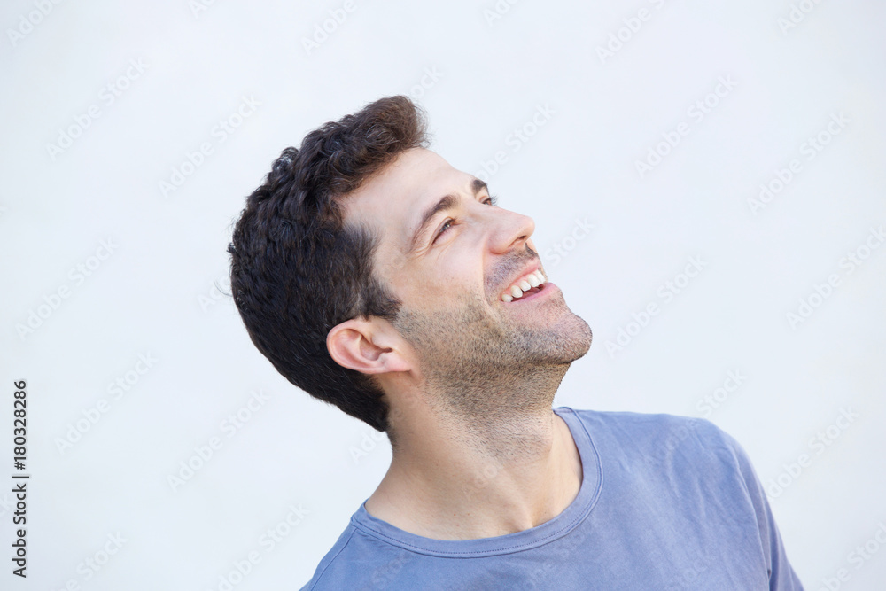 Close up cheerful young man smiling and looking away against white background Close up cheerful young man smiling and looking away against white background