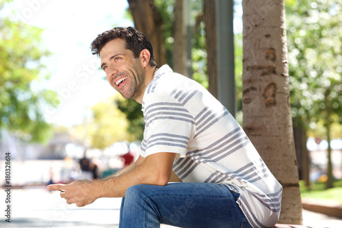 Handsome young man sitting outdoors with mobile phone and laughing © mimagephotos