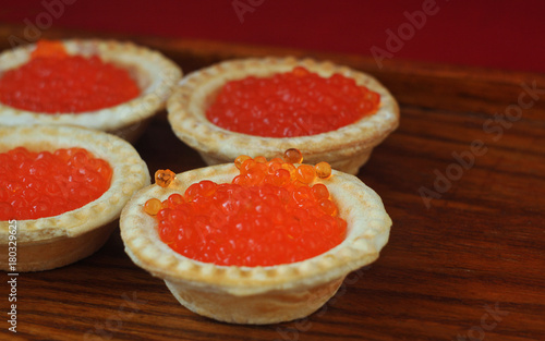 Tartlets with red caviar on a wooden plate.