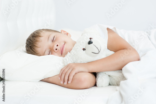 Little boy sleeping in bed with toy bear