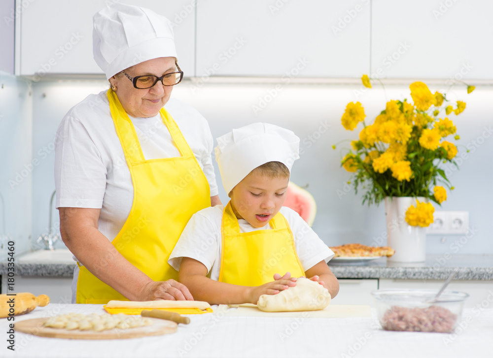 Happy grandmother teaches the child to knead the dough in the kitchen Happy grandmother teaches the child to knead the dough in the kitchen