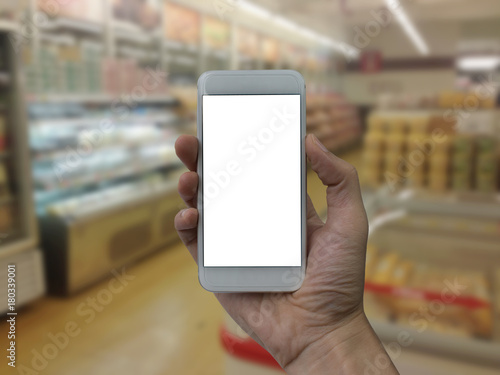 Hand holding smartphone with white blank screen over blurred supermarket and retail store in shopping mall interior background for product display montage