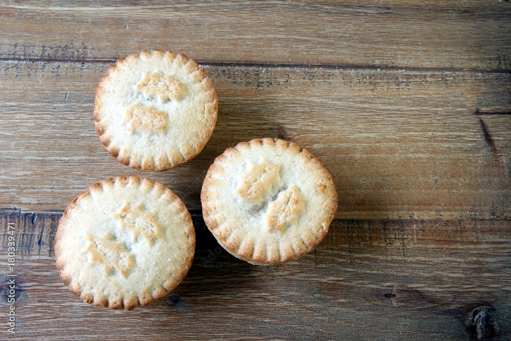 Overhead shot of three mince pies on a wooden table, a traditional Christmas dessert. Copy space for text Overhead shot of three mince pies on a wooden table, a traditional Christmas dessert. Copy space for text