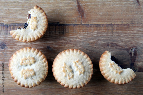 Overhead shot of four mince pies, a traditional Christmas dessert, arranged neatly on a wooden table with two partly eaten. Copy space for text