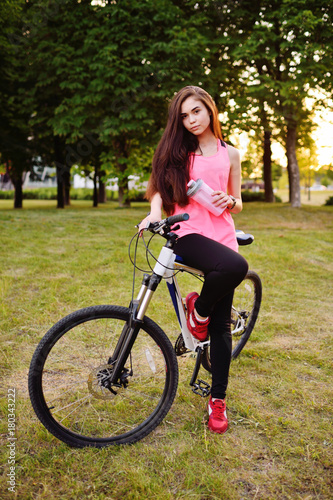 Pretty girl with a bike on a bike ride with a bottle of water or a protein cocktail on the background of nature