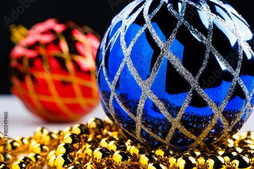 Blue christmas ball on golden garland with blurred decorated red ball on background