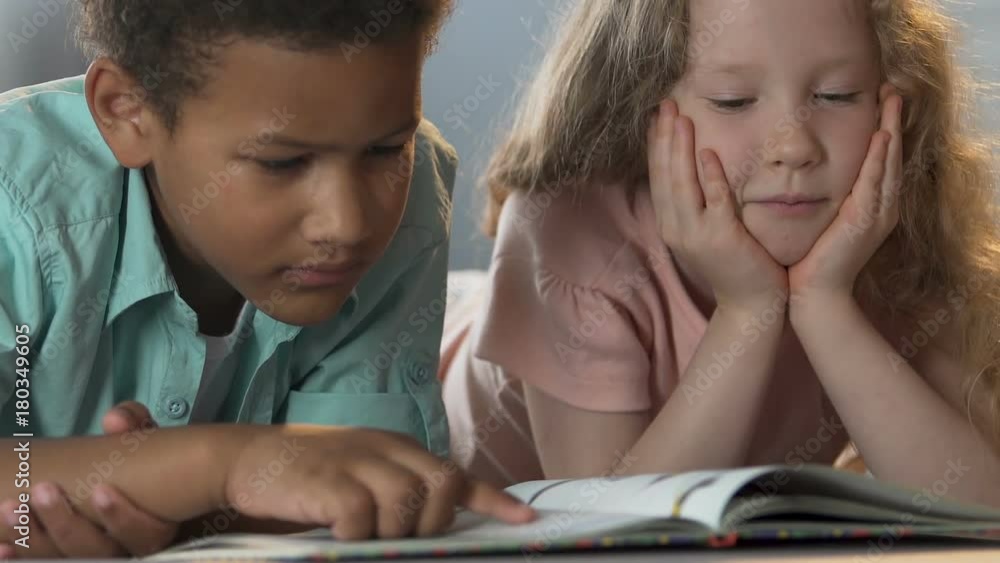 Kids lying next to each other, boy reading book, exchanging looks, friendship Kids lying next to each other, boy reading book, exchanging looks, friendship