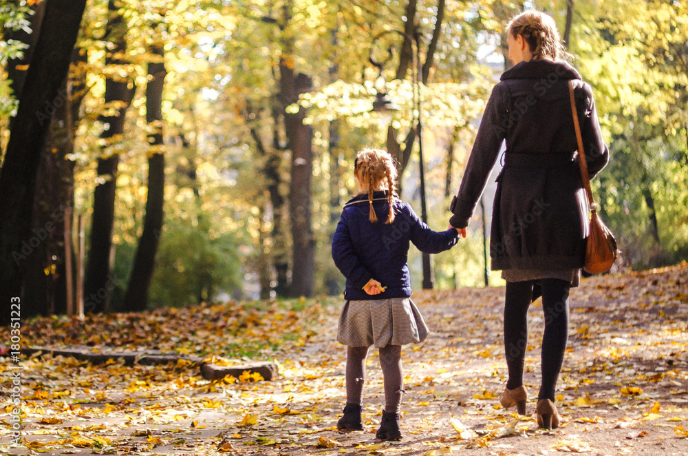 Fototapeta premium Mother with daughter walking in the park in autumn holding hands