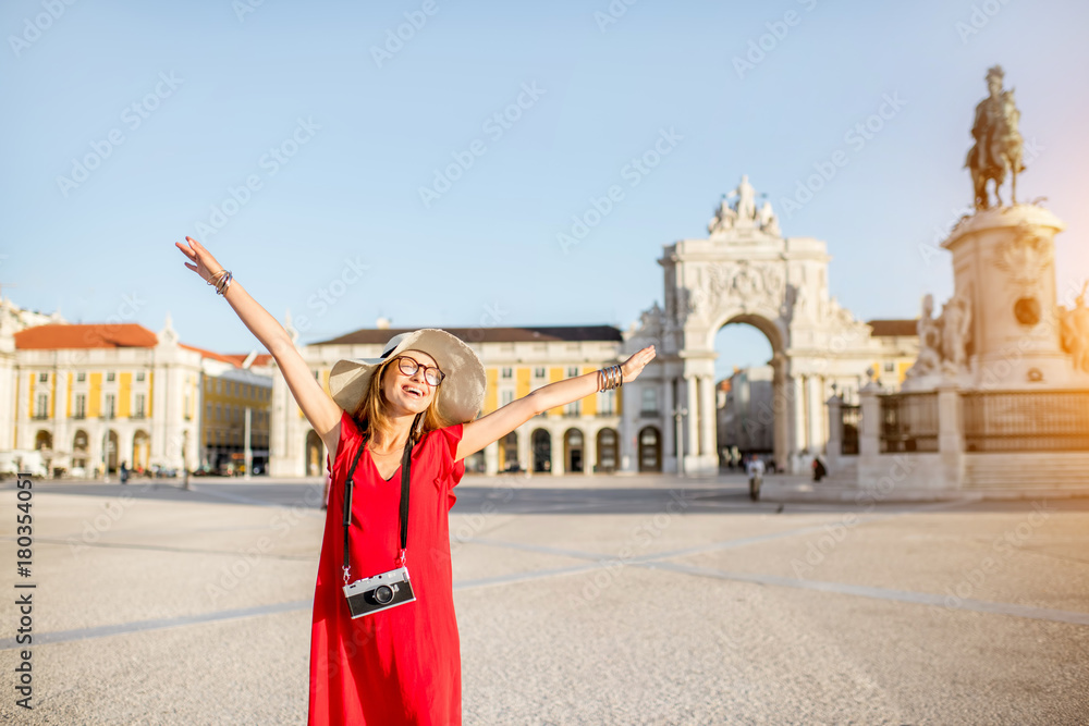 Lifestyle portrait of a young woman tourist standing on the main square with statue and triumphal arch on the background during the morning light in Lisbon city, Portugal