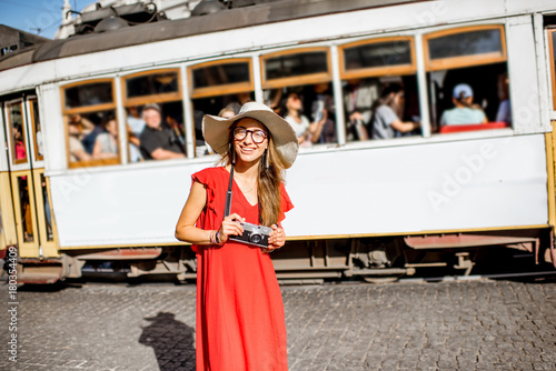 Portrait of a young woman traveler in red dress standing on the street with famous tourist tram on the background in Lisbon, Portugal