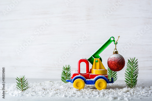 A small toy car is a crane. New Year and Christmas background. Mini Christmas trees from real spruce. Santa Claus made of paper. A blank for a postcard or a poster.