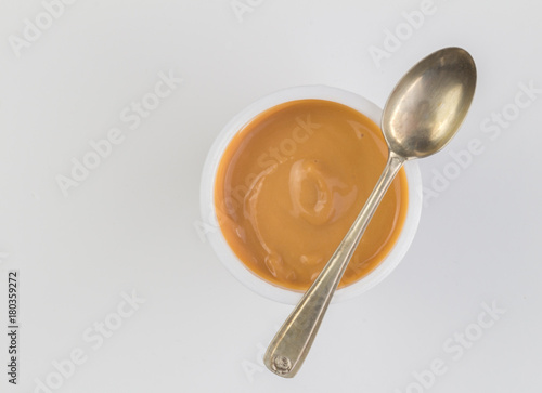 Yogurt background top view shot of caramel flavoured yoghurt in plastic cup with small silver spoon isolated on white background - close up image with space for text