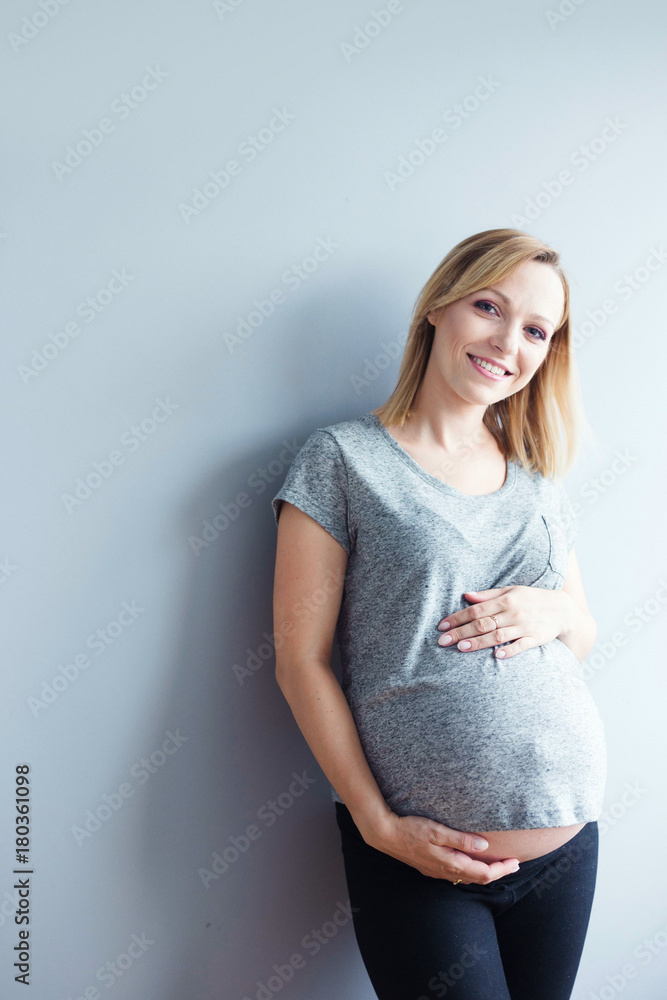 Young pregnant woman standing against gray wall, smiling. Young pregnant woman standing against gray wall, smiling.
