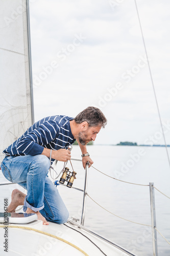 man sits on bow of  sailing yacht and looks overboard