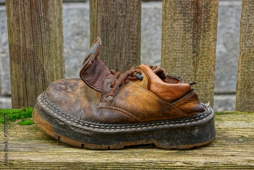 Старый рваный ботинок коричневого цвета на серой доске