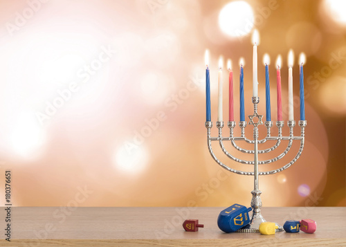 Hanukkah Jewish holiday background with menorah (Judaism candelabra)  burning candles and traditional Dreidrel game toy on wood table and on autumn bokeh sun flare