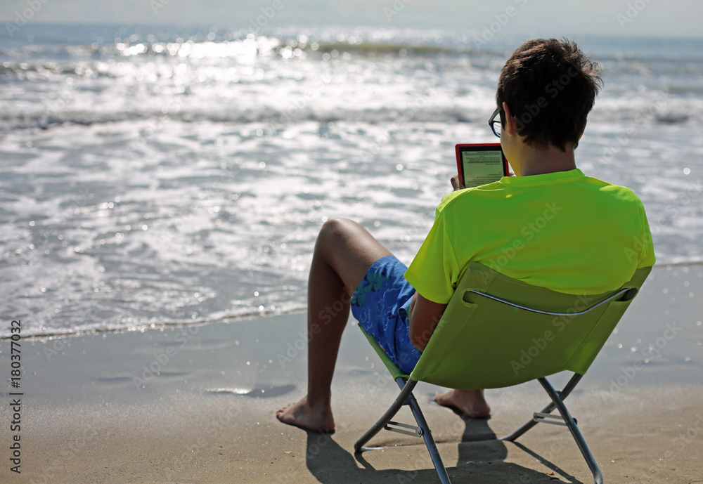 boy reads an ebook sitting on the beach chair
