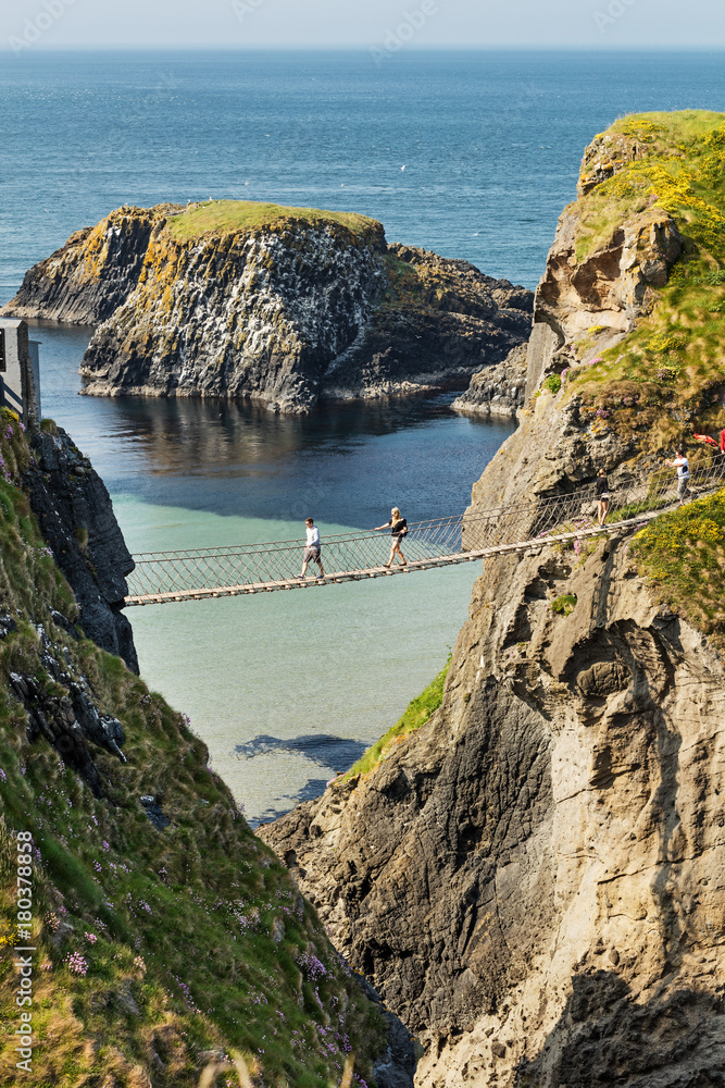 Thousands of tourists visiting Carrick-a-Rede Rope Bridge in County Antrim  of Northern Ireland, hanging 30m above rocks and spanning 20m, linking  mainland with the tiny island of Carrickarede Stock Photo
