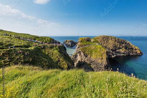 Thousands of tourists visiting Carrick-a-Rede Rope Bridge in County Antrim of Northern Ireland, hanging 30m above rocks and spanning 20m, linking mainland with the tiny island of Carrickarede photo