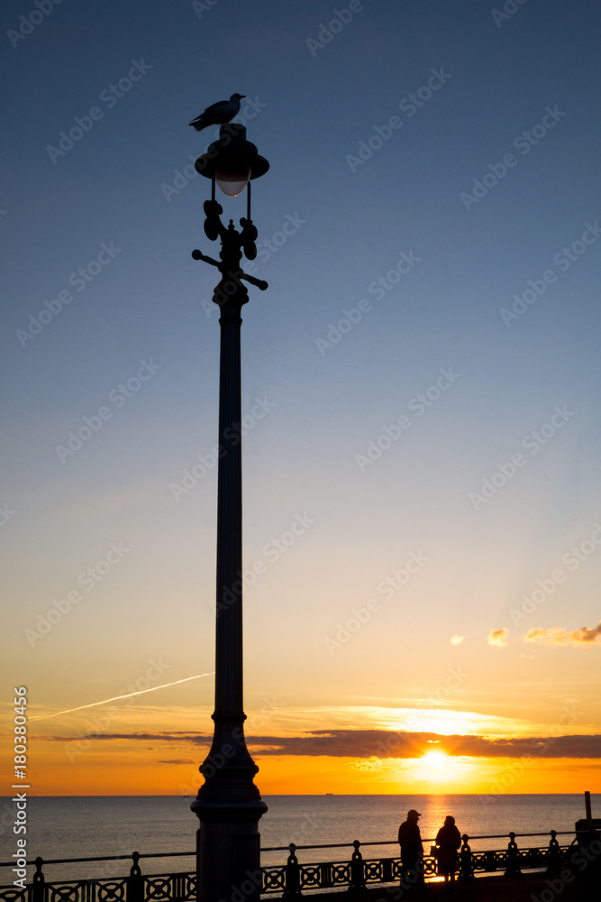 sunset on Brighton seafront promenade, with a silhoutted lamp post and a silhouette of an old couple sunset on Brighton seafront promenade, with a silhoutted lamp post and a silhouette of an old couple