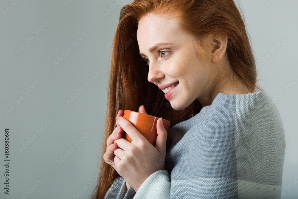 beautiful young girl with a smile with red hair drinks a drink and warms them and a warm blanket beautiful young girl with a smile with red hair drinks a drink and warms them and a warm blanket