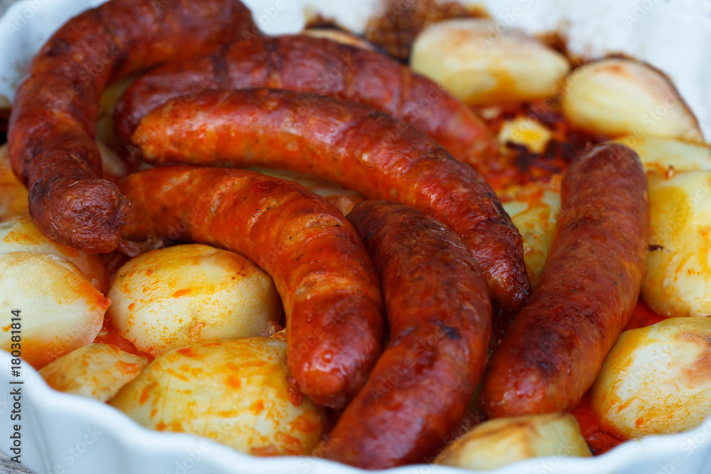 Spicy sausages and potatoes roasted in white roasting tray. Delicious food. Spicy sausages and potatoes roasted in white roasting tray. Delicious food.