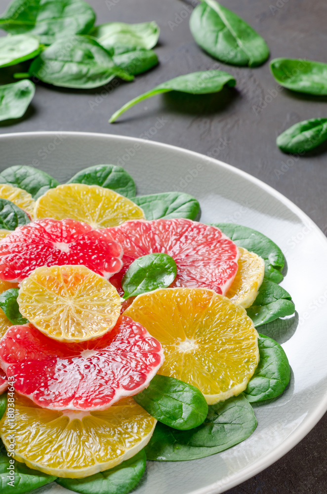 Salad made of orange and grapefruit slices and spinach leaves on a gray plate on dark stone background. Close-up, vertical image