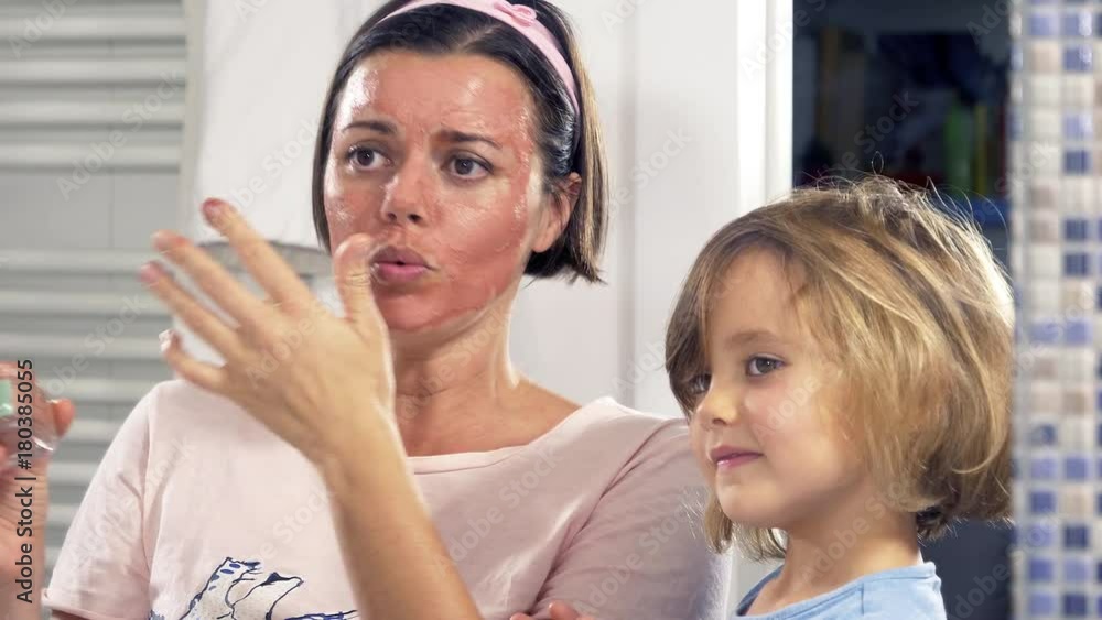 Woman in bathroom applying beauty mask playing and laughing with blond daughter closeup Woman in bathroom applying beauty mask playing and laughing with blond daughter closeup
