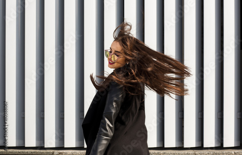 Lifestyle portrait of pretty young model in sunglasses with hair blowing in wind walking at the street