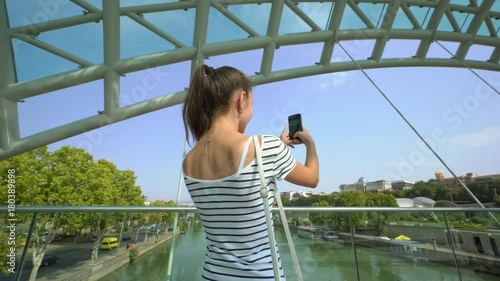 A young lady taking photos on the riverbridge in the city. Medium shot. photo