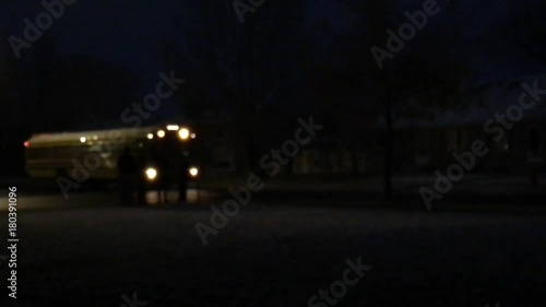 School bus picks up kids on a dark morning with lights flashing randomly about.  