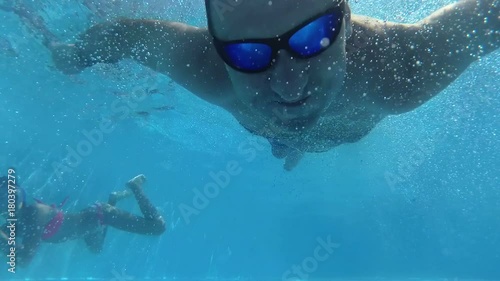 happy man dive under the water in the pool looking into the camera and smiling, slow motion