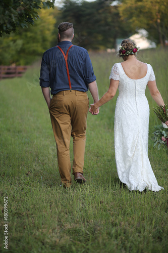 Hipster Wedding Bride and Groom Walking Hand in Hand Through a Field