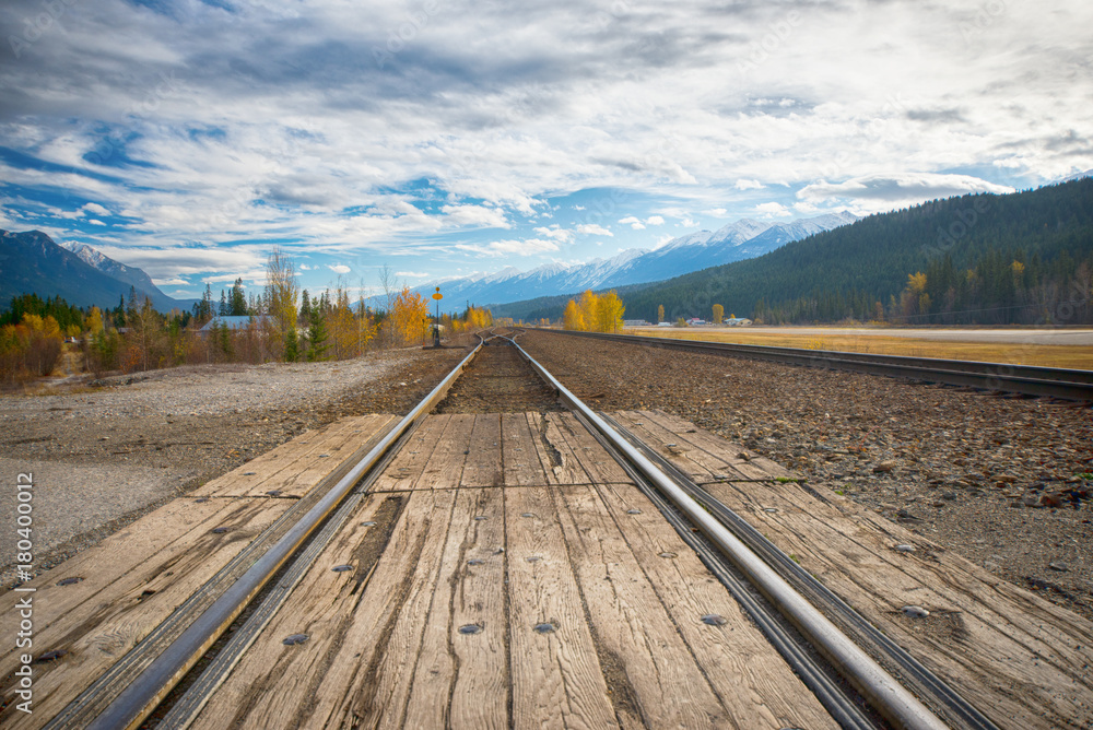 Fototapeta premium Railroad tracks in the horizon with the Canadian Rocky Mountains in the background, taken from Golden, BC