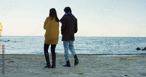 Young couple strolling on the beach. Cold cloudly weather. Sea horizont. Outdoor. From back. photo