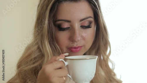 Wallpaper Mural Young teen girl with long hair in a knitted sweater standing with a Cup of tea at home near the window. Blonde girl with make-up drinking tea, close-up. Torontodigital.ca