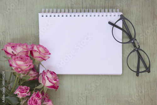 Blank notebook mock up for artwork with pink roses. Place for text. Fresh flowers and black glasses.