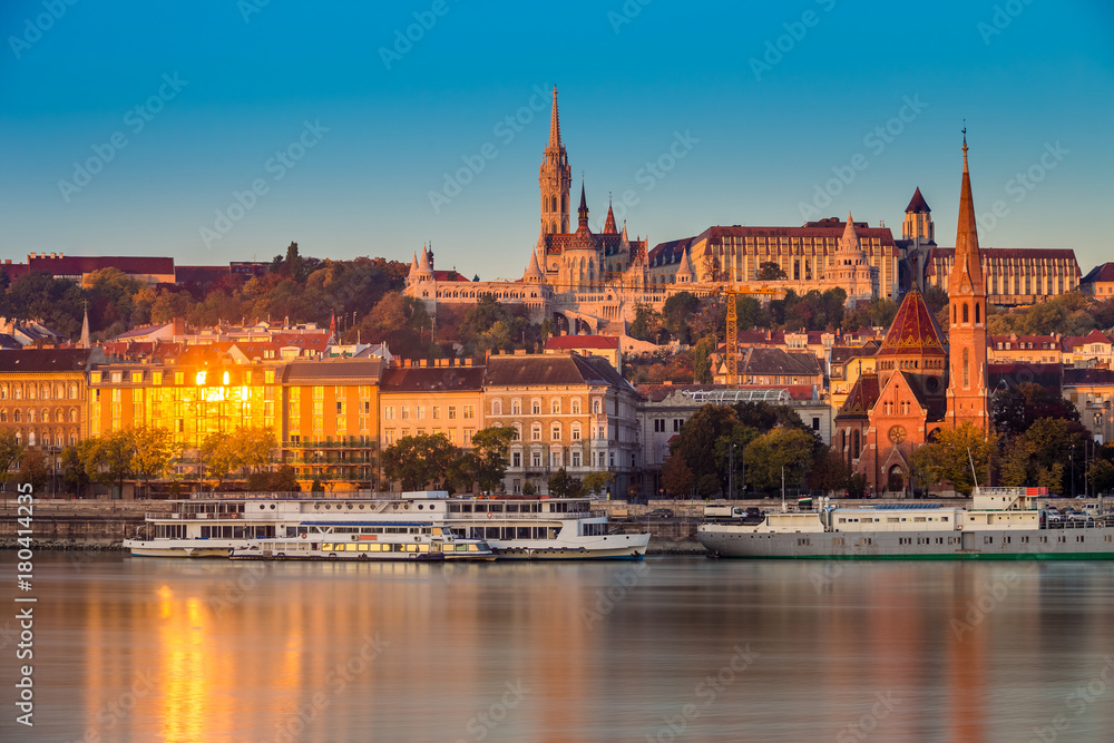 Budapest, Hungary - Golden hour in the morning with the Buda Castle, St. Matthias church and the Fisherman's Bastion with old ships on River Danube and clear blue sky